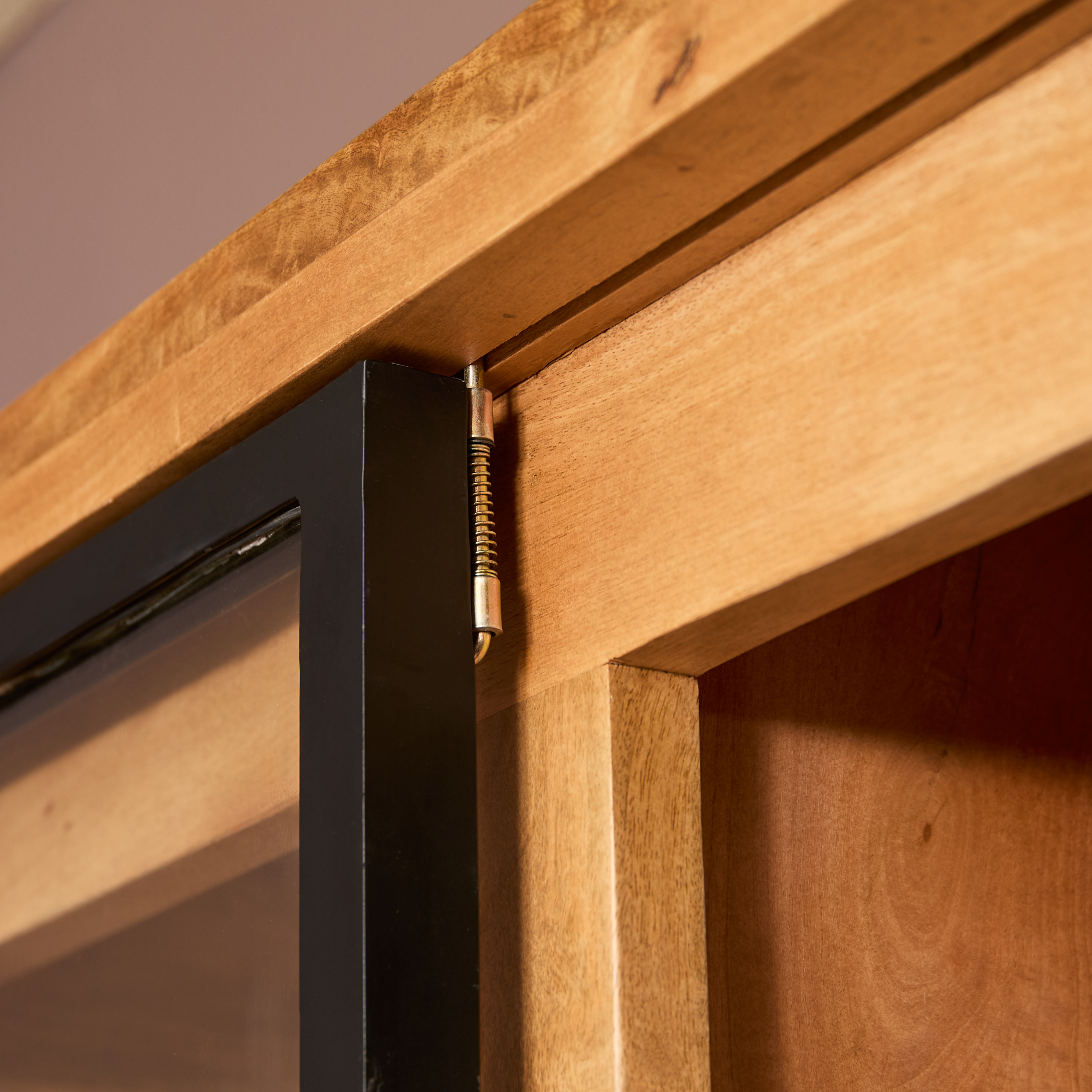 Close-up van een metalen veerscharnier in de Nashville Vitrinekast | 120 cm, bevestigd aan de hoek en waardoor de zwartomrande glazen deur soepel open en dicht gaat.