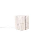 De TRIO Tafellamp TREASURE is een lichtgekleurde houten kubuslamp met zichtbare houtnerf, een kleine ronde knop aan de voorkant en een wit koord dat uit de achterkant steekt, afgebeeld tegen een witte achtergrond.