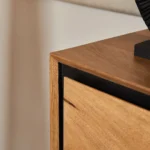 Close-up van de Sidetable RichWood 180 cm, met de gladde natuurlijke houten afwerking en subtiele zwarte afwerking. Een zwart decoratief object rust op het oppervlak tegen een neutrale achtergrond.