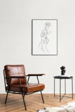 Een moderne, minimalistische kamer met een bruine leren fauteuil en de Bijzettafel CAROLINA van Mirrors and More die een decoratieve sculptuur vasthoudt, plus een lijntekening in een zwarte lijst op de witte muur erboven.