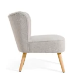 De Fauteuil Vive - Bouclé Naturel is een moderne accentstoel met natuurlijke bouclébekleding, een gebogen rugleuning en schuine houten poten, vanaf de zijkant weergegeven tegen een witte achtergrond.