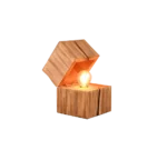 De TRIO Tafellamp TREASURE heeft een gloeiende lamp in een doos met natuurlijke houtstructuur en een gedeeltelijk open deksel, waardoor warm licht naar binnen schijnt.