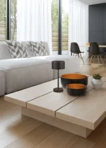 Moderne woonkamer met een lichthouten salontafel, REALITY Tafellamp JEFF, twee schalen en een potplant. Een grijze bank met geometrische kussens en een eettafel met donkere stoelen verschijnen op de achtergrond. Grote ramen vullen de kamer met natuurlijk licht.