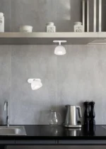 Een moderne keuken met grijze stenen muren, een zwart aanrechtblad, roestvrijstalen gootsteen, waterkoker, glazen kannetje, zout- en pepermolens, gelabelde blikken voor thee, koffie en rijst op een plank en twee REALITY Tafellamp MAXIMA plafondlampen.