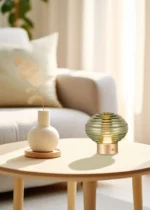 Een moderne woonkamer met een beige bank, een ronde salontafel van licht hout met een witte vaas met gedroogde bloemen en de REALITY Tafellamp EARL in groen geribbeld glas, alles badend in helder natuurlijk zonlicht.