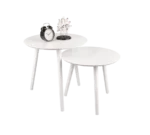 De Mirrors and More Bijzettafel VILANA set bestaat uit twee ronde witte nesttafels met schuine poten. De hoge tafel is gestyled met een zwarte wekker en een klein wit bloemstuk; de onderste tafel is leeg gelaten.