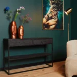 Een moderne kamer met de Sidetable New York | 2 lades in zwart, twee koperen vazen met bloemen, een beige fauteuil, een gouden staande lamp en een ingelijst portret tegen een donkergroene muur.