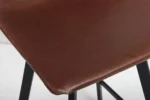 Close-up van Barstoel 'Ozan' PU Bruin zitting met zichtbare stiksels op bruin leer en gedeeltelijk zichtbare zwarte metalen poten (set van 2 per doos).