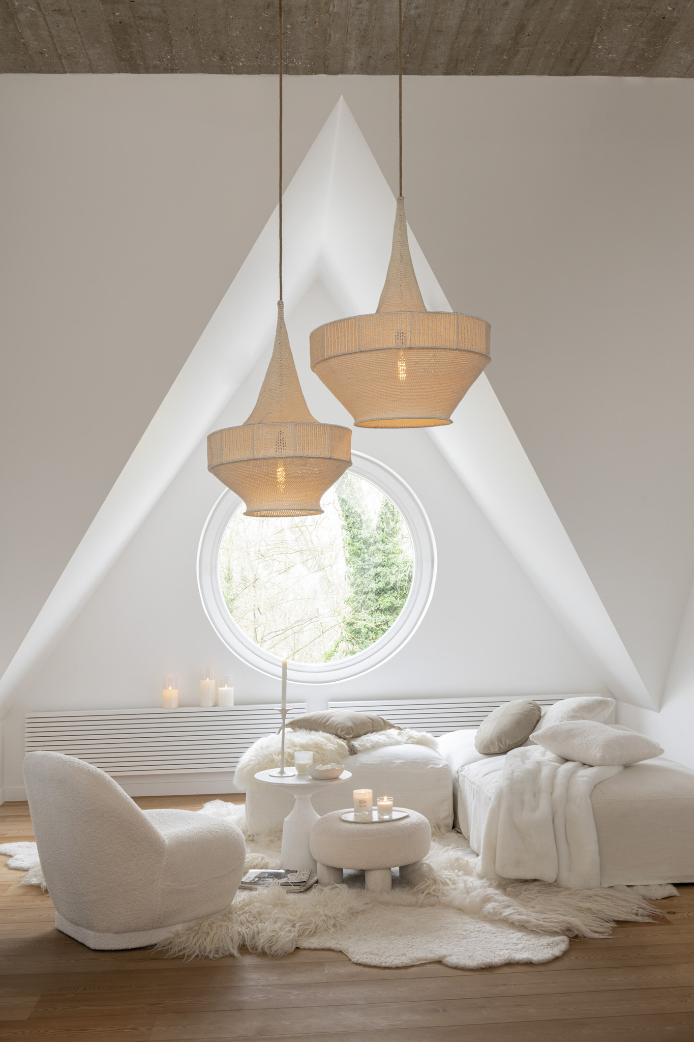 Minimalistische witte woonkamer met de Kruk Teddy Bouclé Wit Zacht, gezellige meubels, rond raam, hanglampen en zacht natuurlijk licht. Neutrale inrichting en pluizige texturen creëren een serene, uitnodigende sfeer.