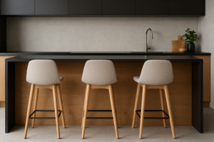 Een moderne keuken met een houten eiland, drie beige barkrukken met houten poten en veel beenruimte, een zwart aanrechtblad, een ingebouwde spoelbak met een strakke kraan en minimalistische zwarte kastjes erboven. Een klein plantje siert het aanrecht.