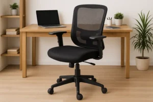 Een zwarte bureaustoel van gaas met armleuningen, een voorbeeld van waar je op let bij het kiezen van een bureaustoel, staat op een houten vloer bij een licht houten bureau met een gesloten laptop, plant en planken in een stijlvolle thuiskantooromgeving.