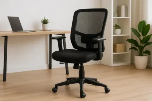 Een zwarte ergonomische bureaustoel met netrugleuning-ideaal om op te letten bij de aankoop van een bureaustoel-staat op een houten vloer voor een bureau met een gesloten laptop en plant, met planken en potplanten op de achtergrond.