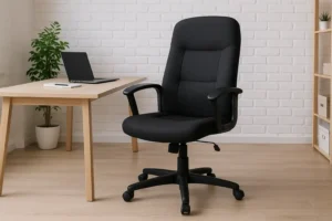 Een zwarte bureaustoel met armleuningen op wieltjes staat naast een houten bureau met een gesloten laptop - perfect voor wie weet waar je op moet letten bij een bureaukast. De ruimte is voorzien van lichte houten vloeren, een witte bakstenen muur en een plant in potten.