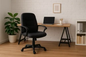 Een modern thuiskantoor met de beste bureaustoel voor thuiswerken - een zwarte draaistoel - voor een houten bureau met een gesloten laptop, notitieblokken en potloden, met een potplant en planken tegen een witte bakstenen muur.