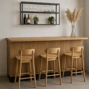 Een minimalistische huisbar met drie houten krukken op de ideale barhoogte, een licht houten aanrecht, een glazen vaas met pampagras en een wandplank met wijnflessen, glazen en kleine potplanten.