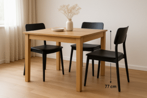 Een houten eettafel met drie zwarte stoelen, één met het label 77 cm hoog-de ideale zithoogte voor een tafel van 77 cm. Een vaas met gedroogde bloemen en gestapelde borden sieren de ruimte in een lichte, minimalistische kamer met houten vloer.