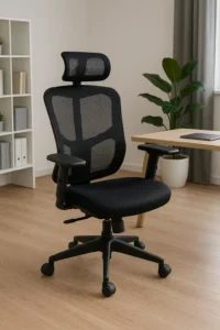 Een moderne zwarte ergonomische bureaustoel met een rugleuning en hoofdsteun van gaas staat naast een houten bureau in een licht, minimalistisch kantoor met lichte houten vloeren, een plant in potten en een boekenplank.