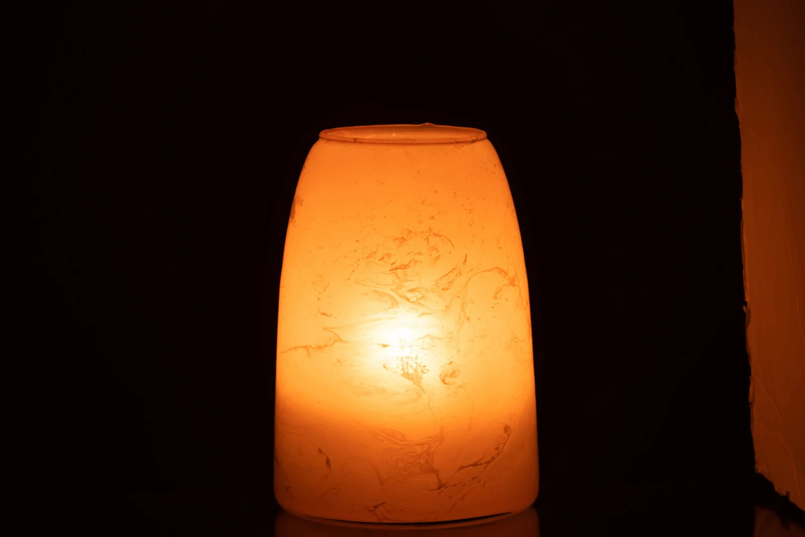 De Theelichthouder Rosa Glas Roze Groot heeft een oplichtend roze glazen oppervlak met een glad, gemarmerd ontwerp, dat afsteekt tegen een donkere achtergrond en een warm, uitnodigend licht werpt.