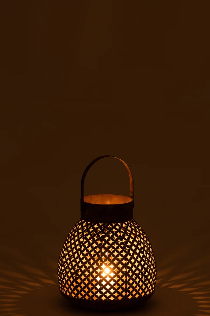 De Kaarsenhouder Lantaarn Bloem Metaal Goud Groot werpt warm, ingewikkeld licht en bloemen schaduwen door het geperforeerde metalen ontwerp, en creëert een gezellige sfeer tegen een donkere achtergrond.