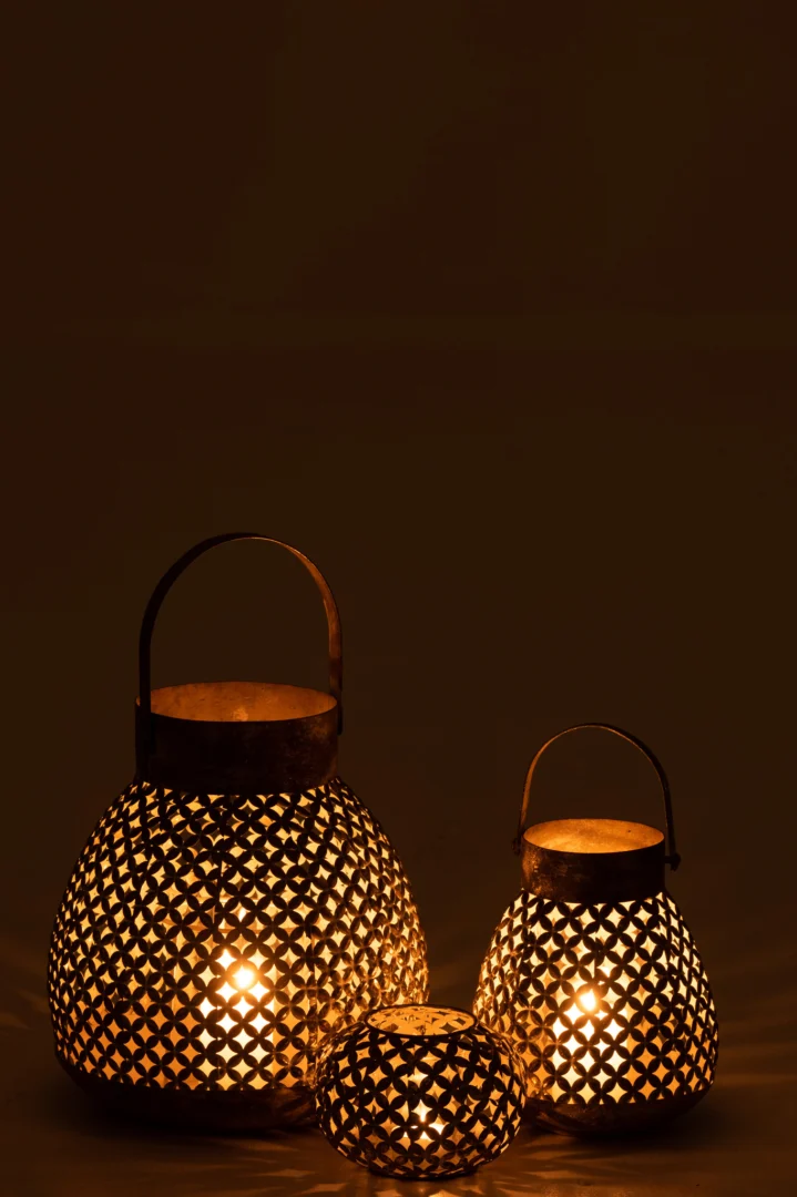 De Kaarsenhouder Lantaarn Bloem Metaal Goud Groot gloeit warm met kaarsen erin en werpt ingewikkelde patronen als hij elegant op een donker oppervlak tegen een donkere achtergrond staat.