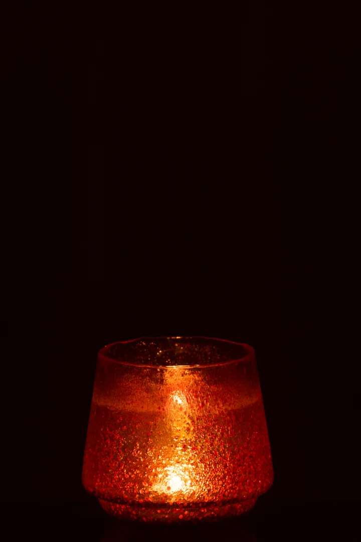 De Theelichthouder Stippen Glas Oranje Groot, een grote oranje glazen kandelaar met gestructureerde stippen, gloeit warm met een brandende kaars erin tegen een donkere achtergrond.