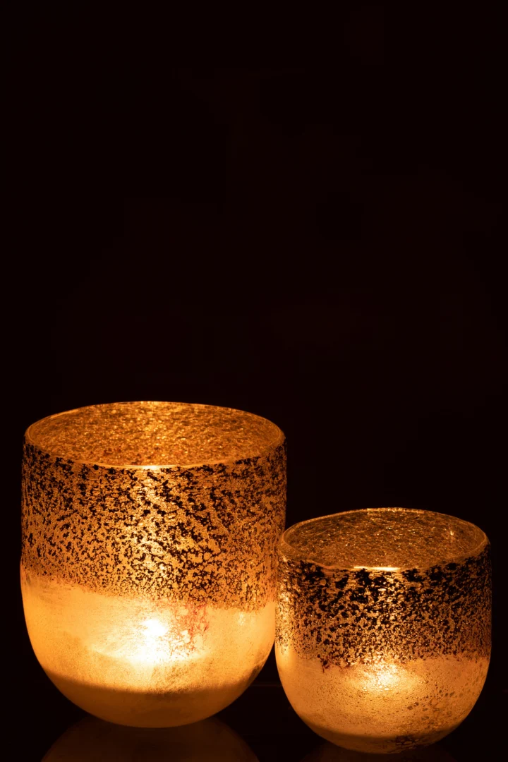 De Kaarsenhouder Orkaan Milano Glas Grijs Roze Groot gloeit warm met een brandende kaars erin, werpt gouden licht en creëert een gezellige, uitnodigende sfeer tegen een donkere achtergrond.