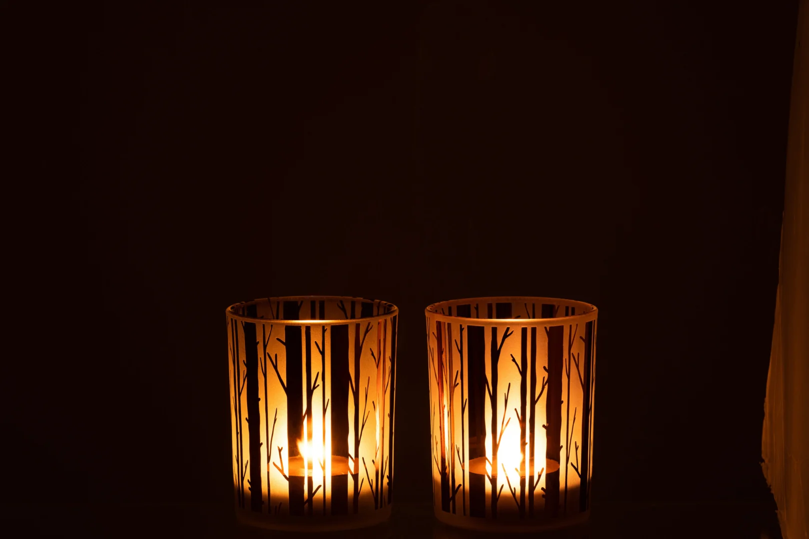 De Kaarsenhouder Orkaan Boom Glas Bruin Medium Set 2 heeft twee bruine glazen kandelaars met een boomtakkenpatroon, die warm oplichten in het donker tegen een zwarte achtergrond.