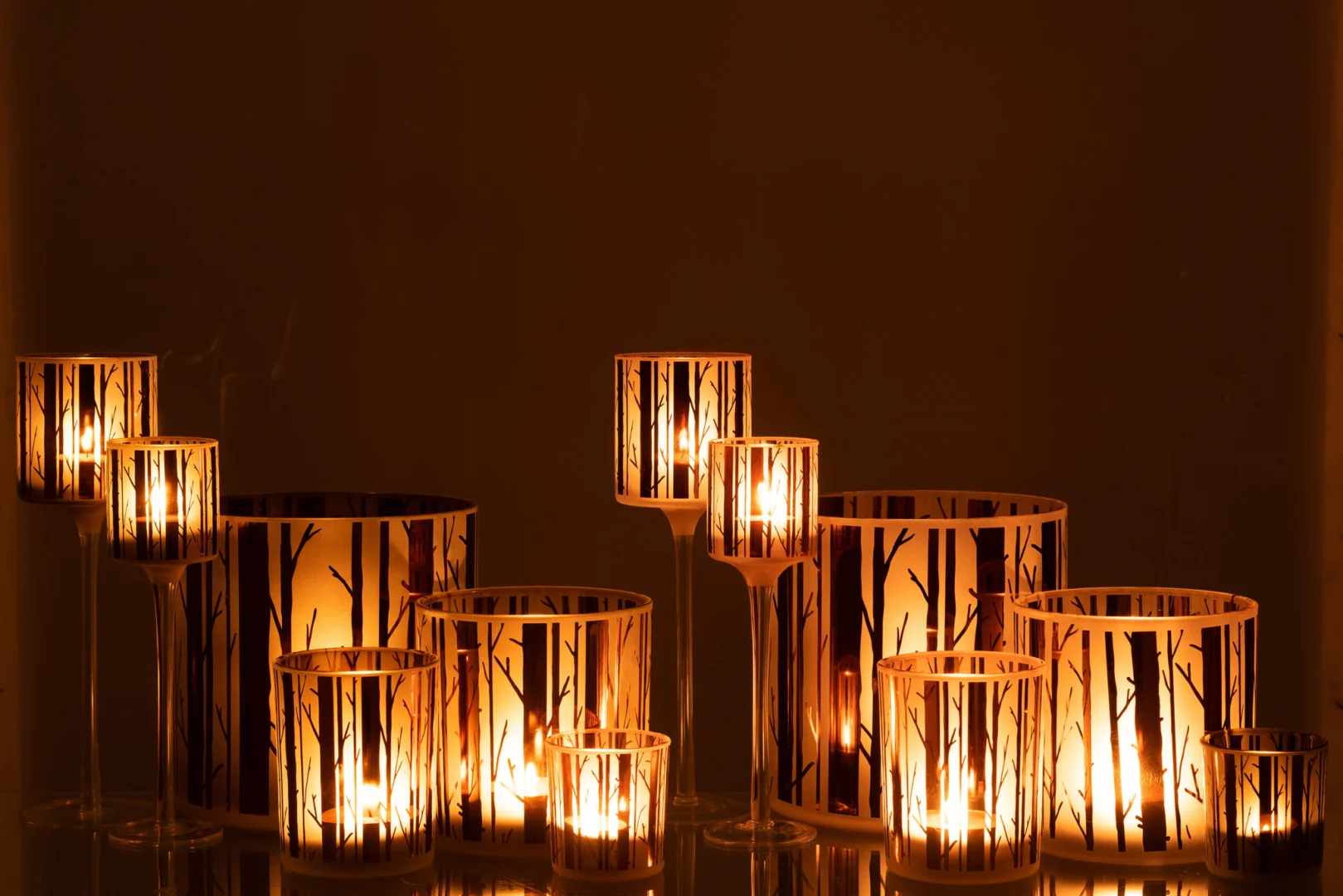 Theelichthouder Op Voet Boom Glas Bruin Groot Set 2 heeft twee grote bruine glazen kandelaars met een boomtakontwerp, die een warme, gezellige gloed in de kamer werpen als ze branden. Hun verschillende hoogtes versterken de uitnodigende sfeer.