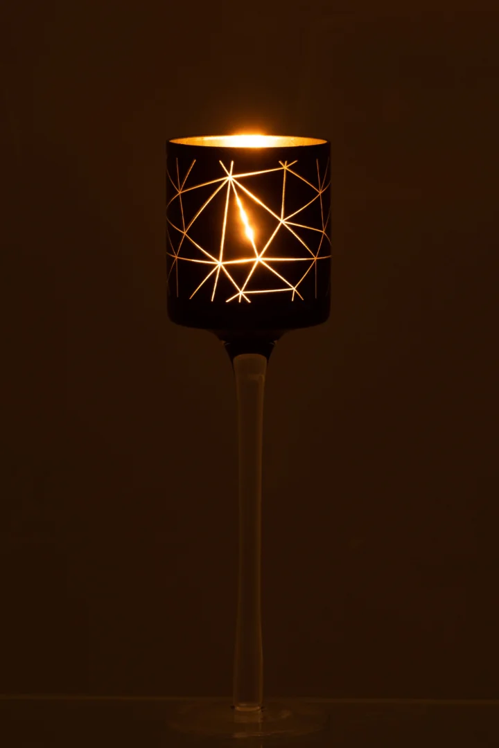 De Theelichthouder Op Voet Milano Glas Zwart Goud Klein Set 2 heeft kandelaars met ster- en lijnuitsnijdingen, die een warme gloed verspreiden terwijl ze op slanke transparante stelen staan, ideaal voor donkere achtergronden.