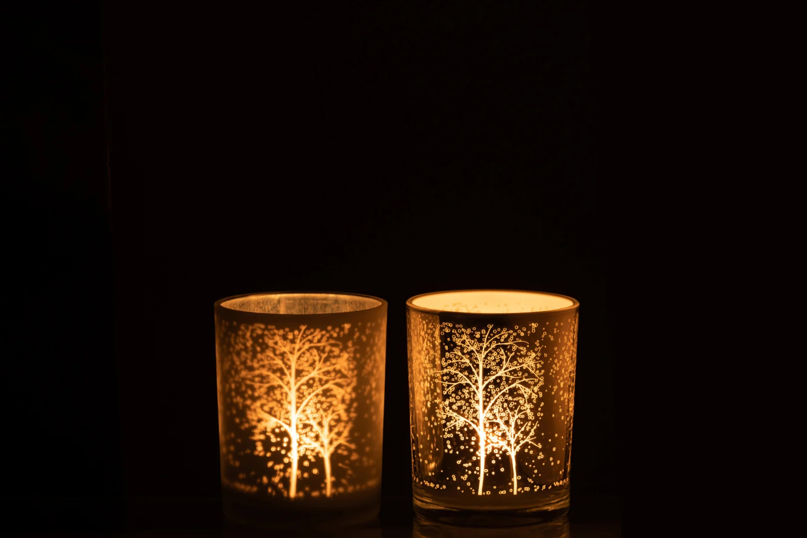 De Kaarsenhouder Orkaan Boom Glas Wit Zilver Medium Set 2 heeft twee glazen kandelaars met oplichtende boommotieven, die een zacht licht werpen en een gezellige, serene sfeer creëren.
