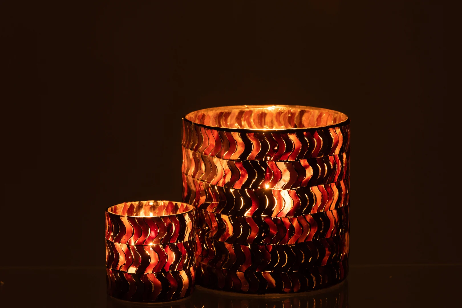 De Kaarsenhouder Orkaan Golf Glas Donkerroze heeft twee kandelaars van verschillende grootte met een golvend, veelkleurig patroon dat warm opgloeit in het donker, zacht, goudkleurig licht werpt en een gezellige sfeer creëert.