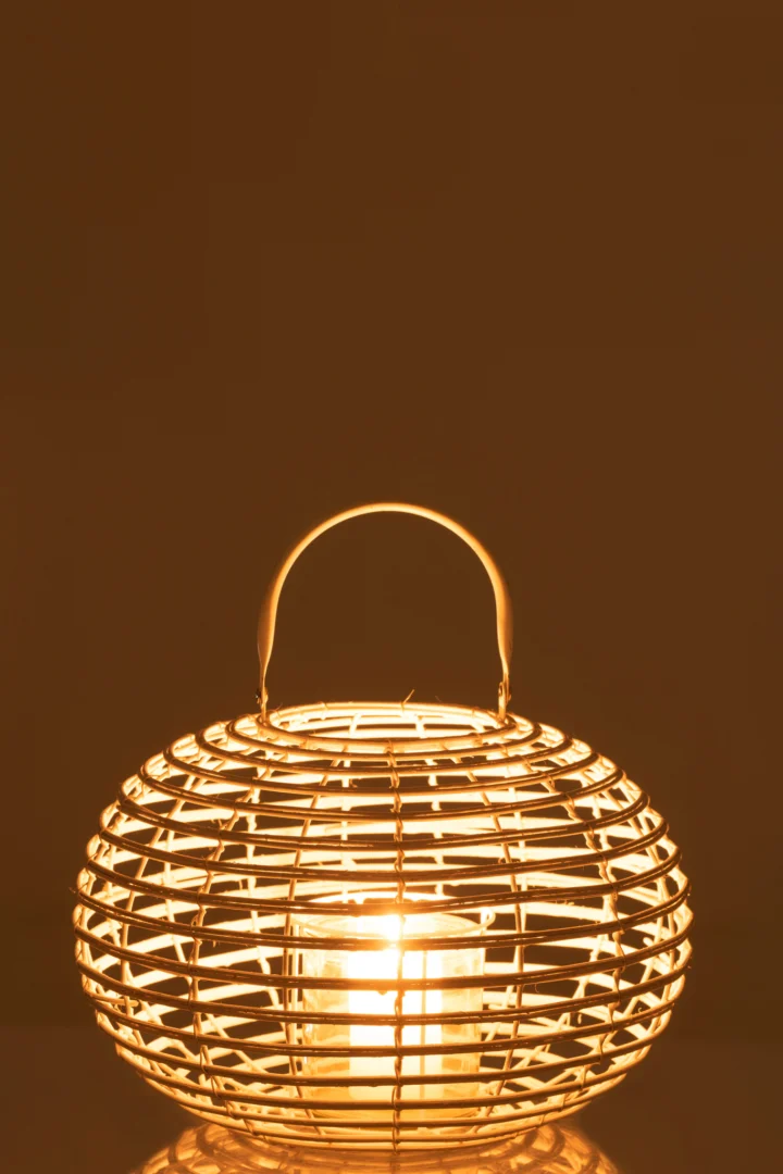 De Lantaarn Rond Bamboe Wit Mat heeft een brandende kaars in het ronde, geweven bamboe ontwerp met een handvat, dat een warme, zachte gloed werpt tegen een effen bruine achtergrond.