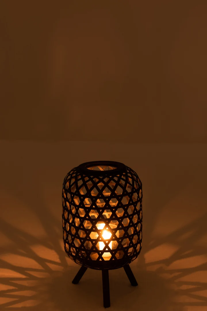 De Lantaarn Birdy Hout Zwart Op Voet werpt ingewikkelde schaduwen op een glad, beige oppervlak als de kaars zachtjes gloeit in een schemerige kamer.