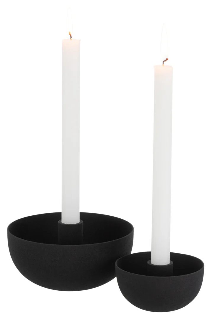 Een brandende witte conische kaars staat in de Kaarsenhouder Schaal IJzer Zwart Groot, een moderne matzwarte ronde houder, tegen een effen witte achtergrond.