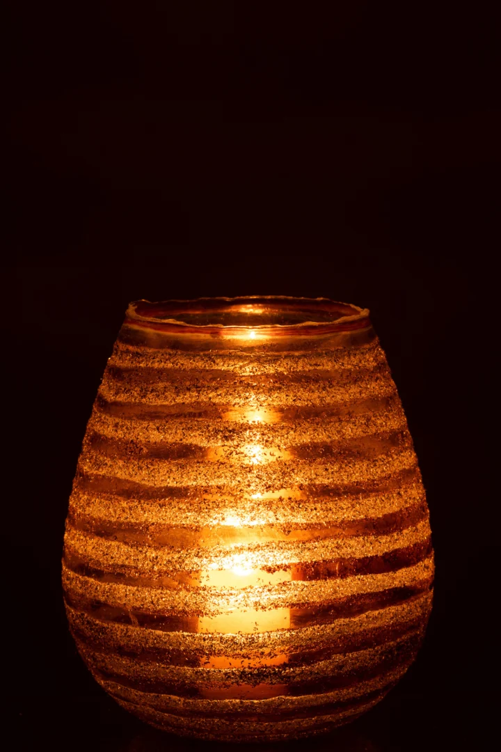 Een gloeiende kaars schijnt in de Theelichthouder Streep Rond Glas Bruin Groot, het ronde, gestreepte glas werpt een warm, gouden licht tegen een donkere achtergrond.
