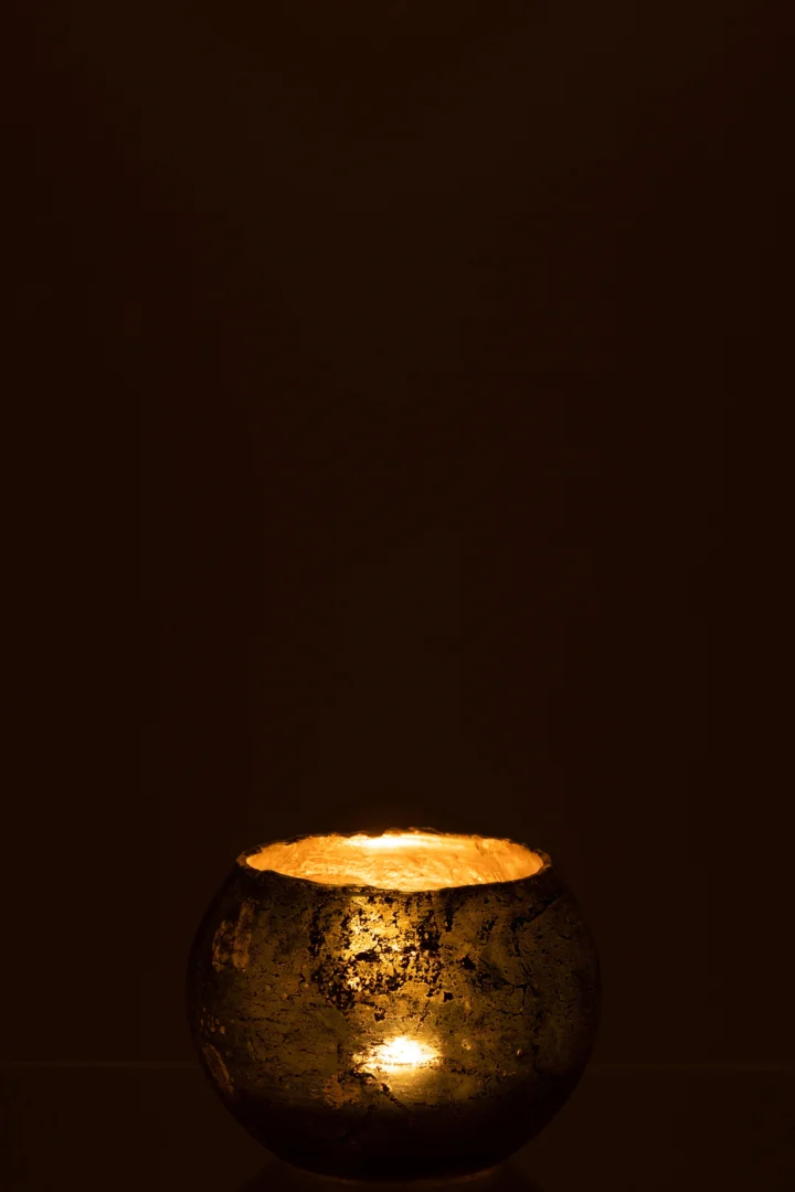 Een enkele brandende kaars in de Theelichthouder Glas Groen Klein gloeit warm in een donkere, minimalistische omgeving en creëert een vredige en gezellige sfeer.