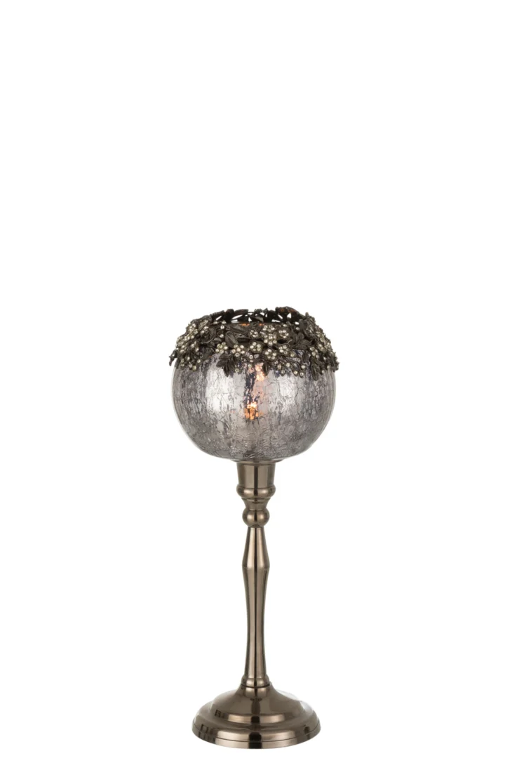 De Theelichthouder Op Voet Juweel Glas Smokey Grijs Groot is een decoratieve kandelaar met een metalen voet, een gebarsten rookgrijze glazen bol en een sierlijke metalen rand met bloemen, afgebeeld tegen een witte achtergrond.
