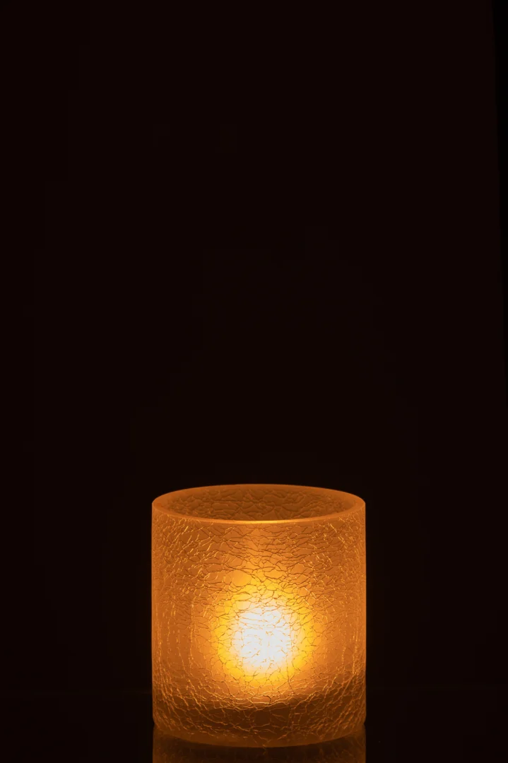 De Orkaan Cilinder Craquelure Glas Mat Wit Klein kaars gloeit warm in de glazen houder met textuur en werpt een zacht licht tegen een donkere achtergrond.