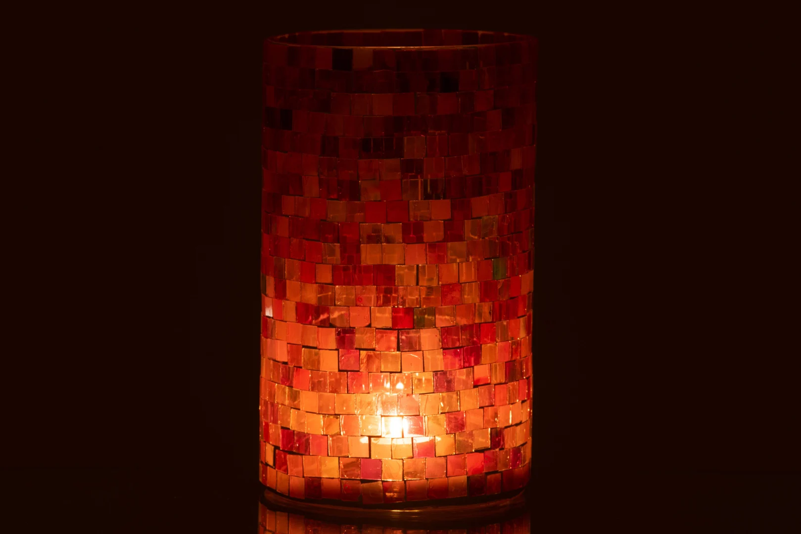 Een brandende kaars gloeit in de Theelichthouder Cilinder Mozaïek Glas Roze Mix Groot, het roze mozaïekglas werpt een warm, sfeervol licht tegen een donkere achtergrond.