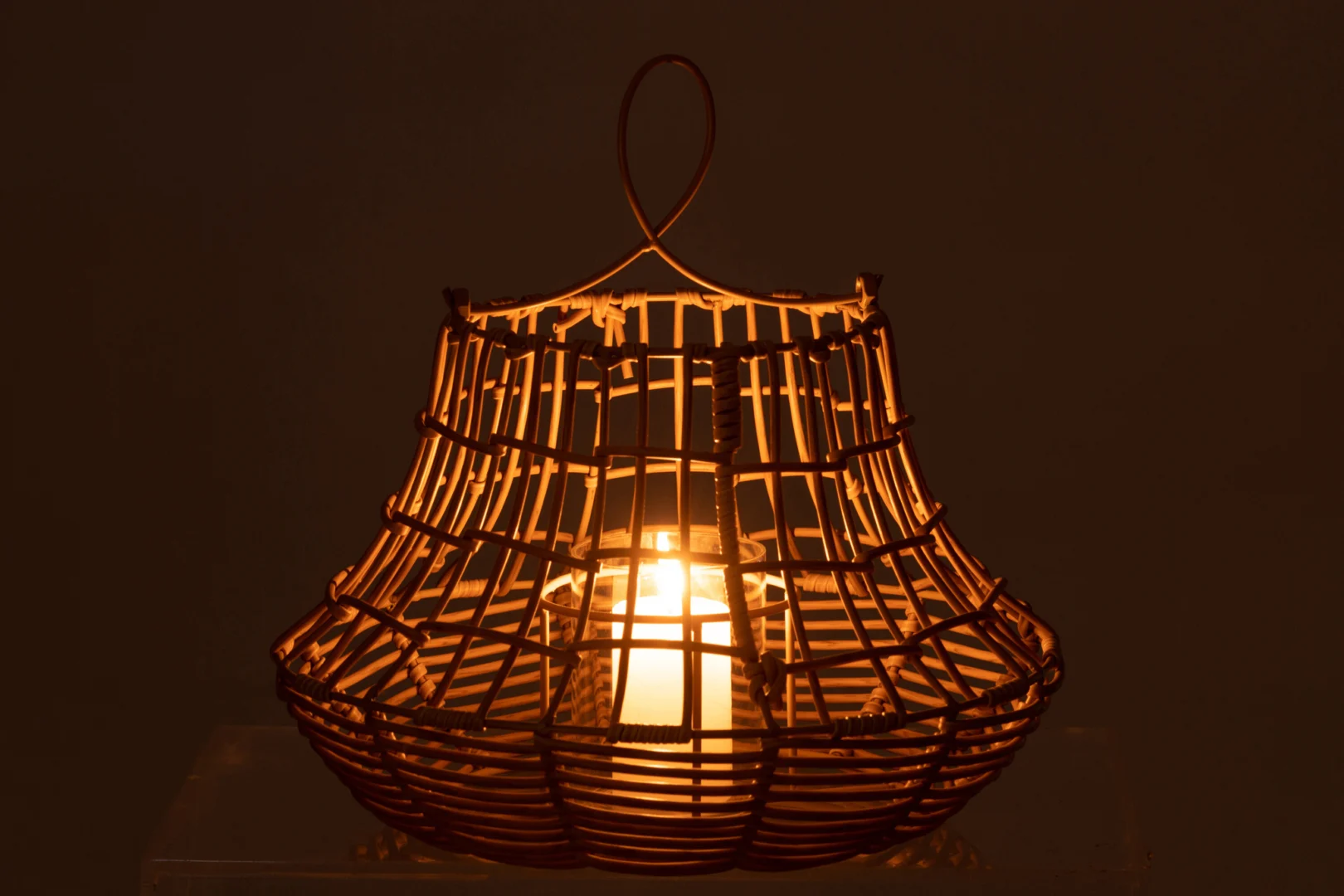 De Kaarsenhouder Orkaan Rotan Hangend Hoog heeft een gloeiend licht in de geweven rotan kap en de lusvormige handgreep, die warm sfeerlicht in het donker werpt.