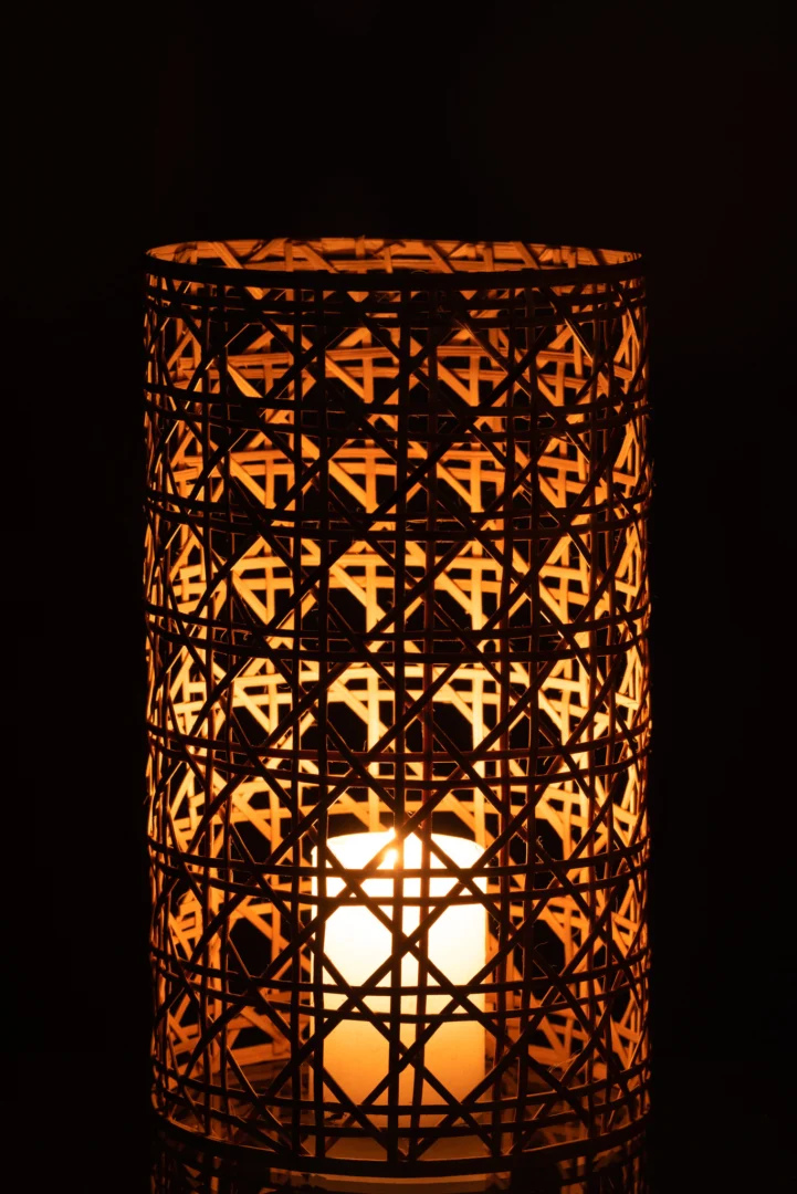 De Kaarsenhouder Orkaan Candice Glas Riet Natuurlijk Groot werpt een warme, gedessineerde gloed in het donker wanneer er een kaars brandt in de cilindervormige houder van bamboe en glas.