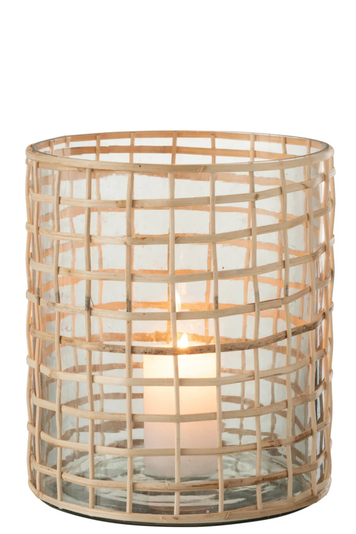 De Kaarsenhouder Orkaan Violet Glas Riet Groot heeft een brandende kaars in een cilindervormige houder van violet glas, gewikkeld in een lichtgekleurd geweven rotanontwerp, dat een zachte gloed door het glas en de buitenste laag werpt.