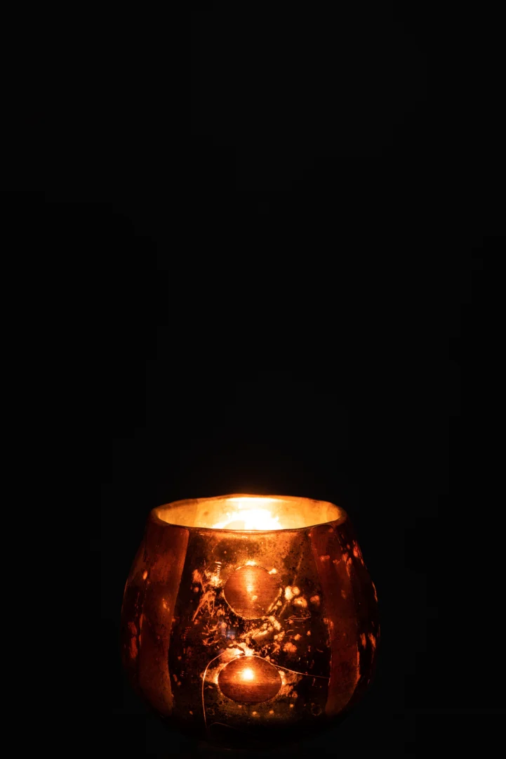 De Theelichthouder Kokos Glas Bruin kandelaar werpt een warme, uitnodigende gloed tegen een donkere achtergrond en creëert zo een gezellige en vredige sfeer.