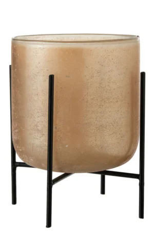 De Kaarsenhouder Orkaan Astor Glas Amber Groot heeft een gematteerde cilindrische beige kaars in een houder van helder glas, geplaatst op een minimalistische zwart metalen standaard met vier poten, tegen een witte achtergrond.