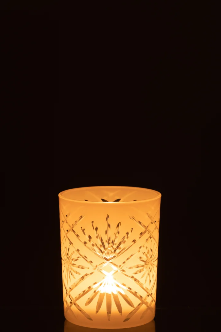 De Kaarsenhouder Orkaan Santorini Glas Wit Medium gloeit warm als er een kaars in brandt. De decoratieve houder werpt sterrenpatronen af tegen een donkere achtergrond.