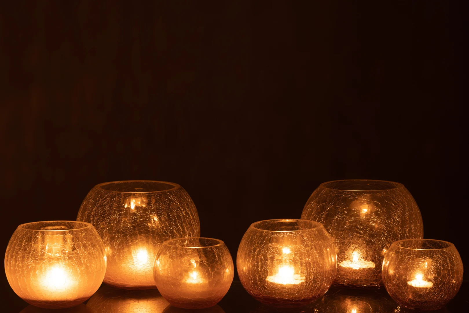 Twee Kaarsenhouder Orkaan Orb Craquelure Glas Paars kandelaars staan op een donker oppervlak, elk met een brandende kaars erin, die een warme paarse gloed werpt tegen de donkere achtergrond.