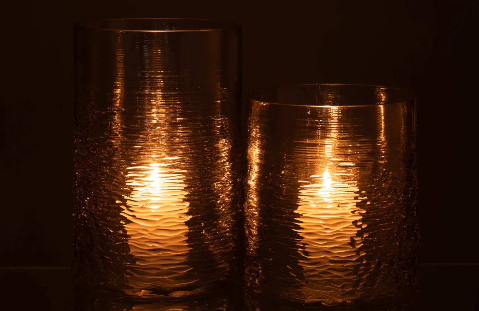 De Kaarsenhouder Orkaan Zeeglas Grijs Groot gloeit warm in het donker en werpt een zacht licht en zachte reflecties door de grijze glazen houder met textuur.