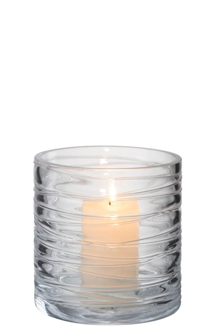 Een brandende witte pilaarkaars staat in de Kaarsenhouder Orkaan Strepen Glas Transparant Klein, een kleine houder van helder glas met horizontale golvende strepen tegen een effen witte achtergrond.