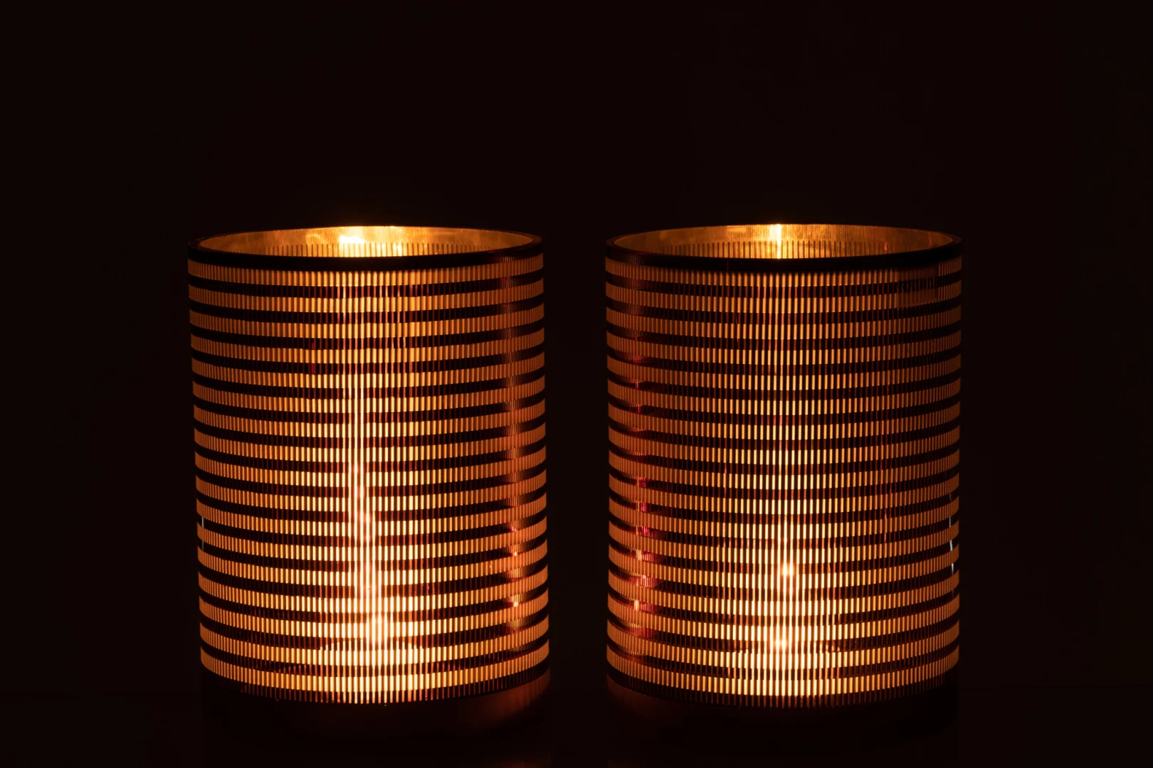 De Kaarsenhouder Orkaan Strepen Glas Bruin Groot is een grote cilindrische kandelaar waarvan de horizontale spleten warm gouden licht door de gedessineerde bruine glazen zijkanten laten schijnen, waardoor een gezellige gloed in het donker ontstaat.