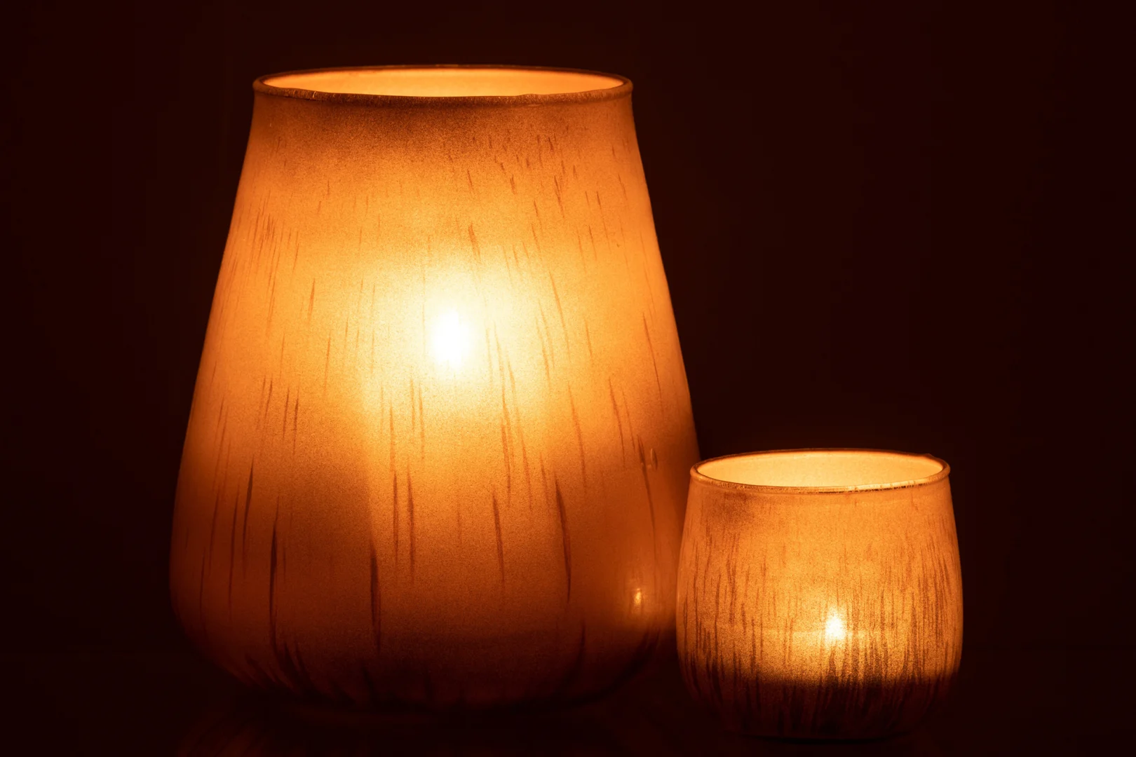 De Kaarsenhouder Hurricane Glas Antiek Bruin Groot, een amberkleurige glazen kandelaar, straalt een warm, zacht licht uit tegen een donkere achtergrond.